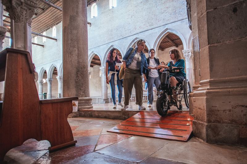 un gruppo di visitatori di cui. una persona in sedia a rotelle percorre la basilica