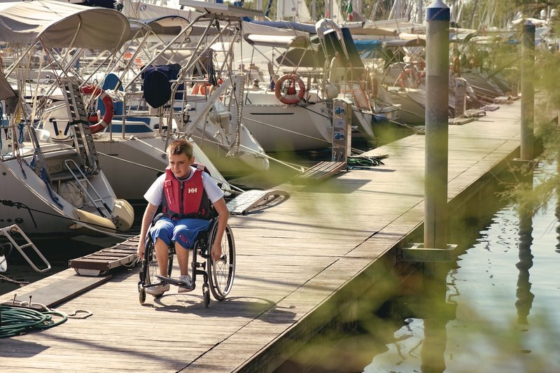 Un ragazzino in sedia a rotelle va verso la barca Hansa per una lezione di vela