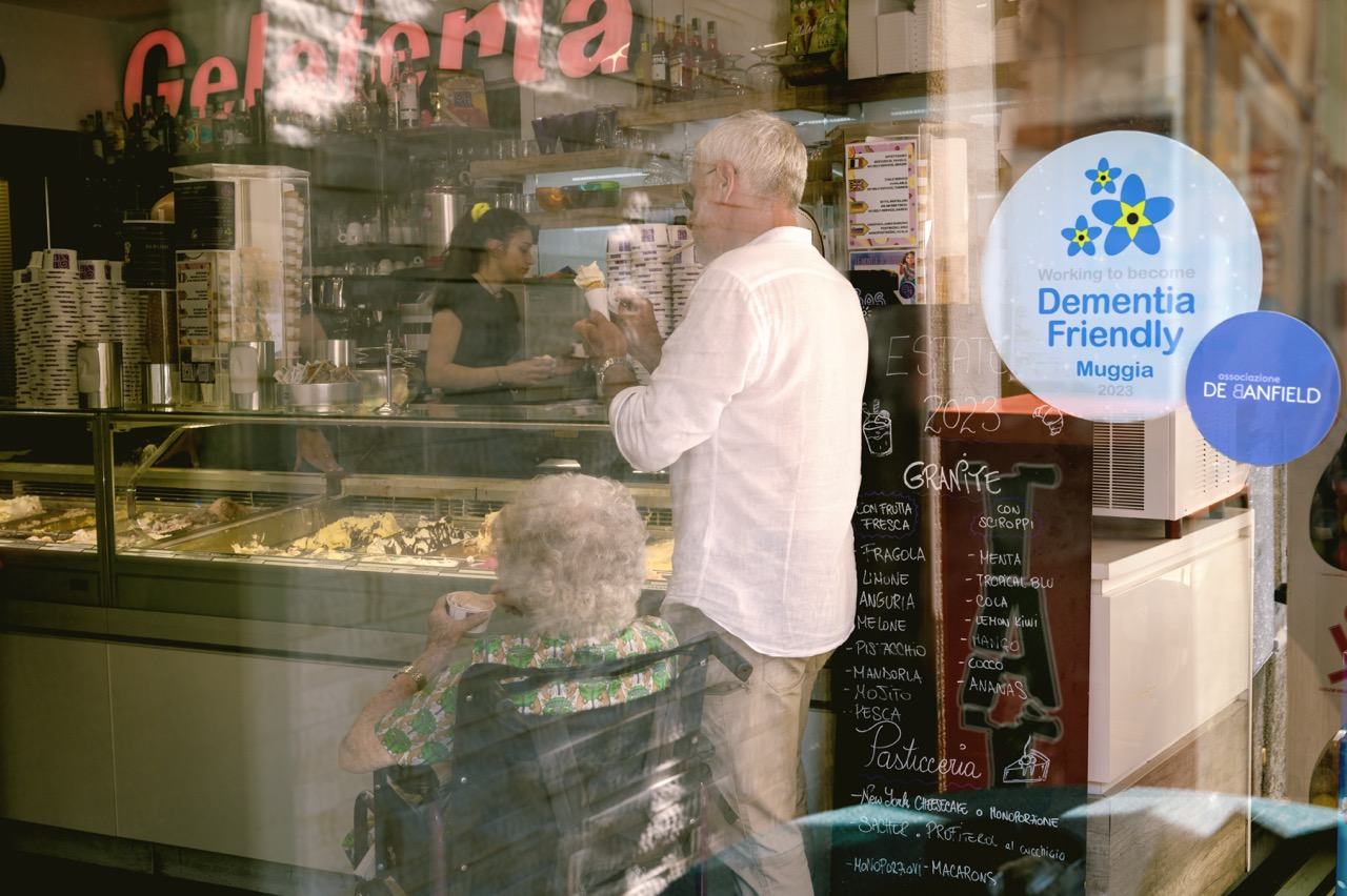 An older lady on a wheelchair with a man accompanying her in a shop in the city of Muggia