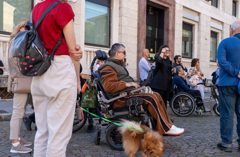 Un uomo in sedia a rotelle e alcune persone ed un piccolo cane esplorano Udine per mapparne l'accessibilità