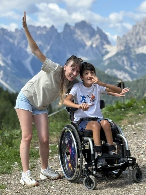 Alice Diana con Luigi, un ragazzo in sedia a rotelle, in posa davanti alle montagne